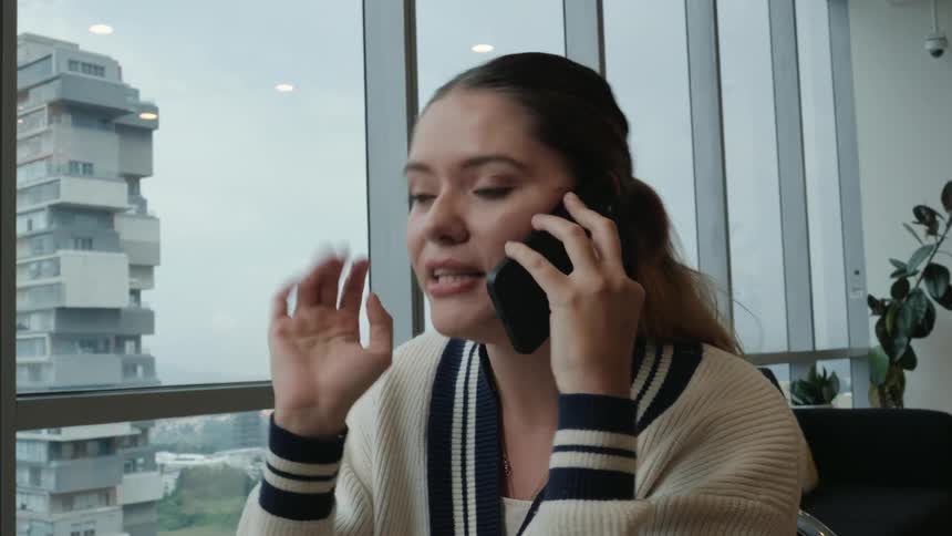 Excited young woman animatedly gossiping on the phone in a modern cafe with a panoramic city view