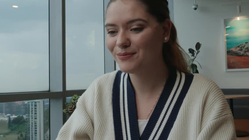 A young professional woman smiles and waves goodbye while on a video call on her laptop in a modern office