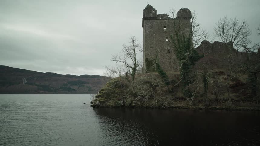 A slow push-in shot of the historic Urquhart Castle ruins on the shore of Loch Ness in Scotland on a gloomy, overcast day
