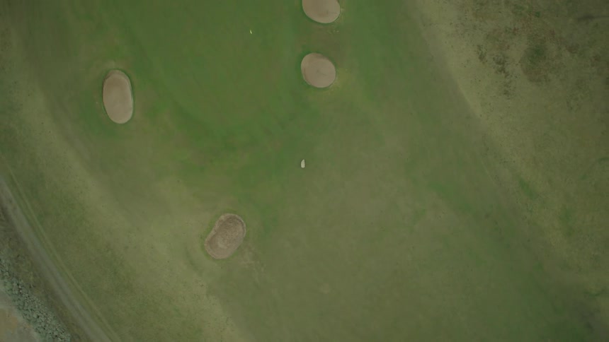 A solitary sheep grazes peacefully on a green field, revealed to be a coastal golf course as the camera pulls up for a stunning aerial view