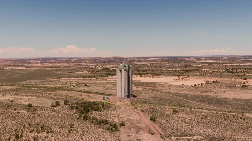An aerial shot slowly pushes in on a towering, isolated grain silo standing alone in the vast, arid desert