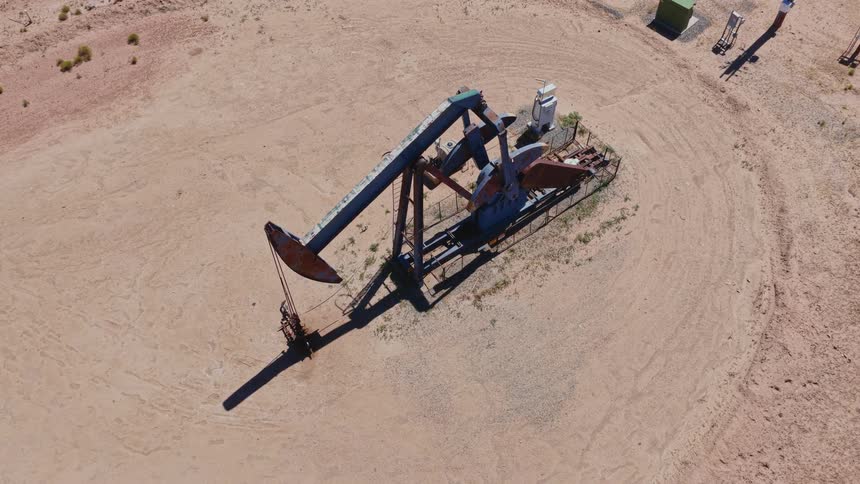 High-angle aerial shot of a rusty oil pumpjack extracting crude oil in a dry, sandy landscape