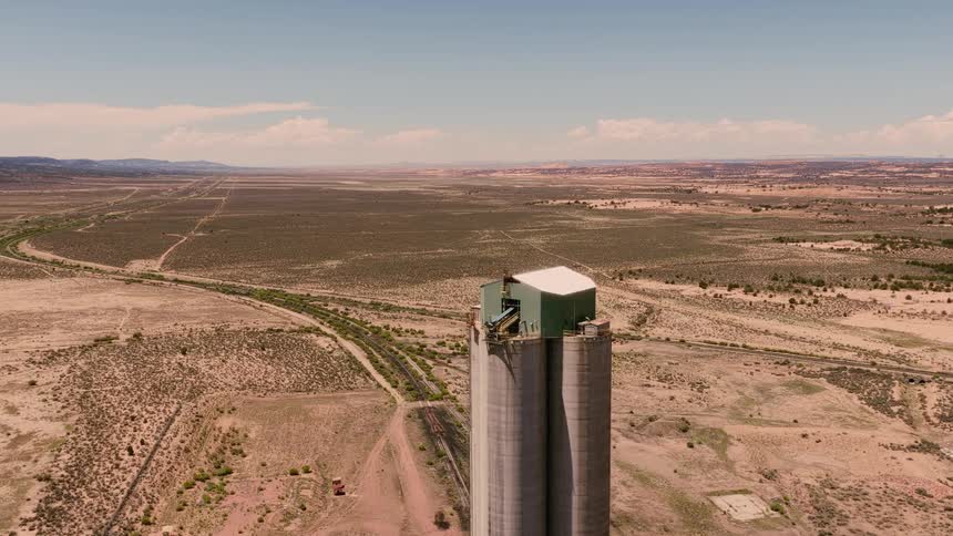 A slow aerial approach reveals an isolated industrial silo standing alone in the expansive, arid plains of the American Southwest