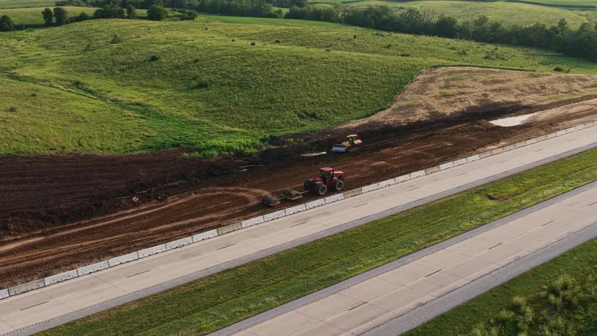 Aerial view of a tractor and bulldozer performing earthmoving work for a construction project alongside a busy highway