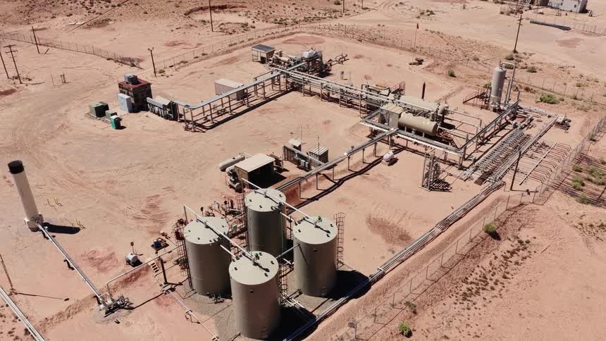An aerial drone flies slowly over a remote oil and gas processing facility located in a vast desert landscape