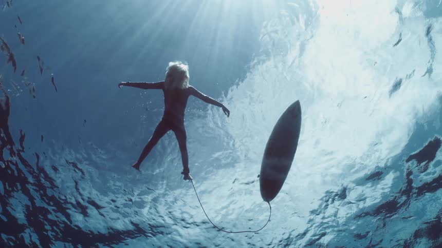 Serene underwater view of a surfer floating peacefully on the surface next to their board as sunlight breaks through the water