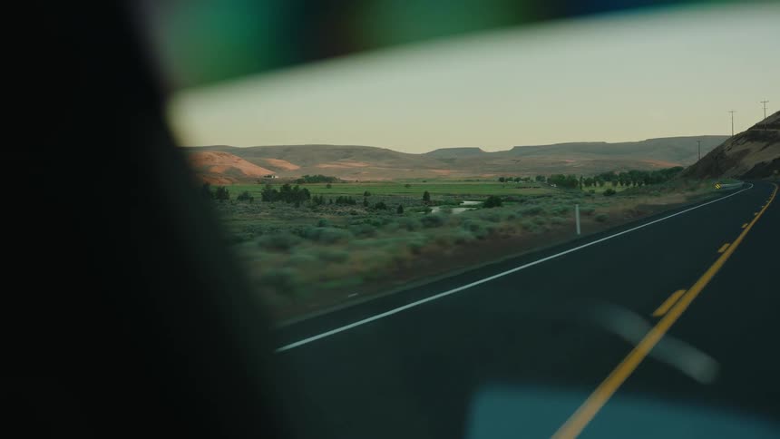 View from a car window driving on a country road past a green valley and rolling hills at dusk