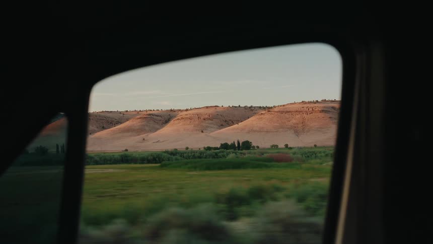 View from a car window of golden rolling hills and a green valley during a scenic drive at sunset