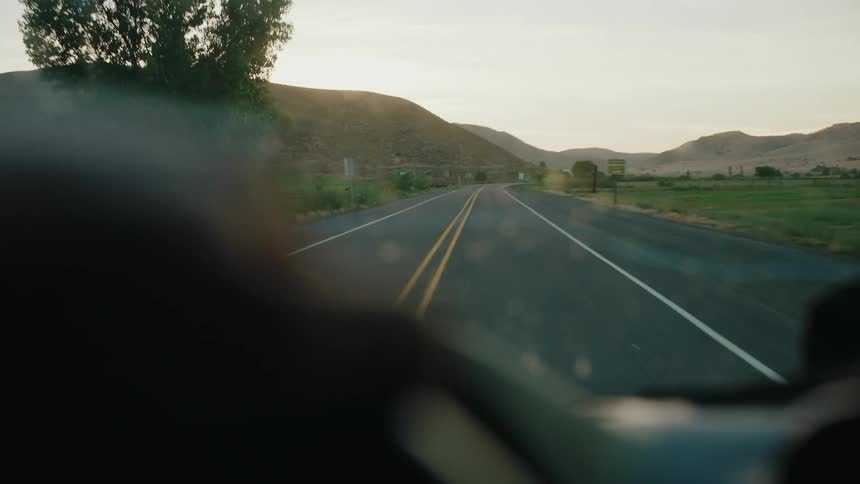 First-person view from a car driving along a scenic country road through rolling hills at sunset