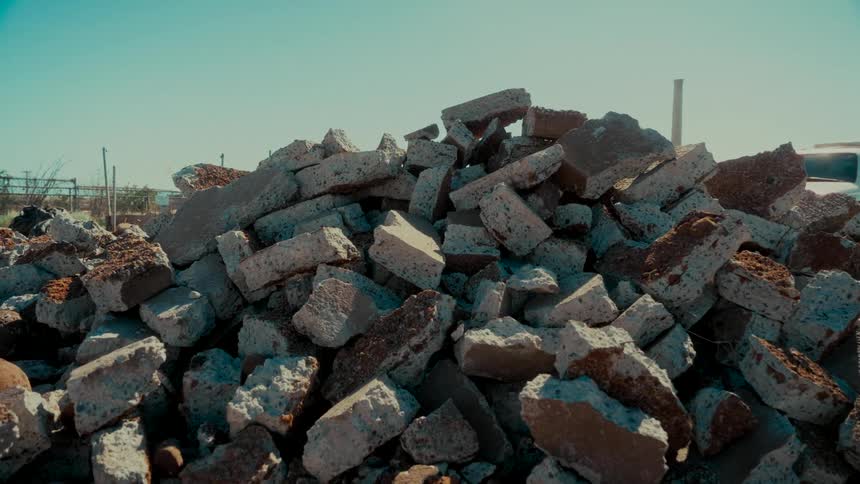 A large pile of broken concrete and rubble sits at a demolition site under a clear sunny sky
