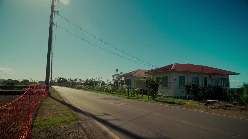 A tranquil, empty road runs alongside a charming coastal home under the bright sun and a clear blue sky