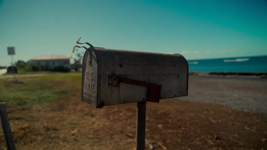 A weathered U.S. Mailbox stands alone in a coastal landscape with the ocean in the background