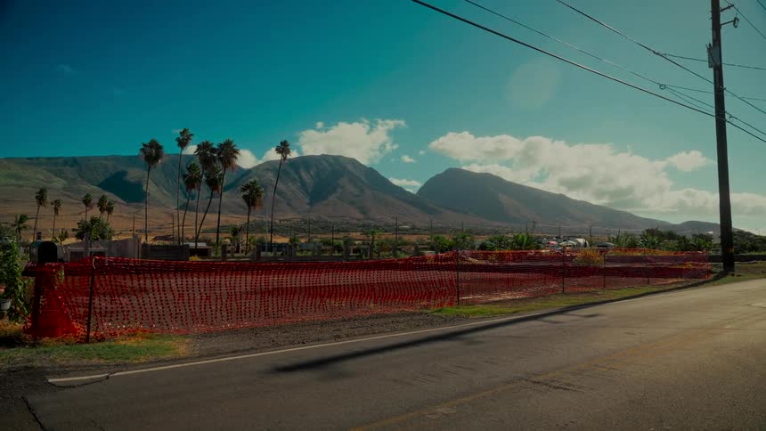 A plot of land cleared after the Lahaina wildfires is fenced off with the West Maui Mountains towering in the background