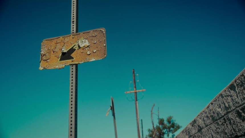 A low-angle shot of a rusty, bullet-ridden arrow sign in a desolate landscape under a clear blue sky