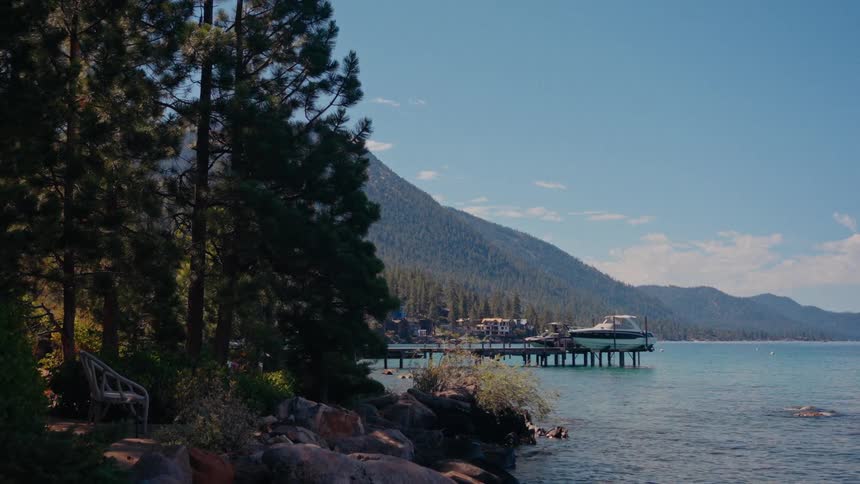 A picturesque view of a serene mountain lake with a pier and a boat on a lift, framed by a rocky shore and tall pine trees under a clear blue sky