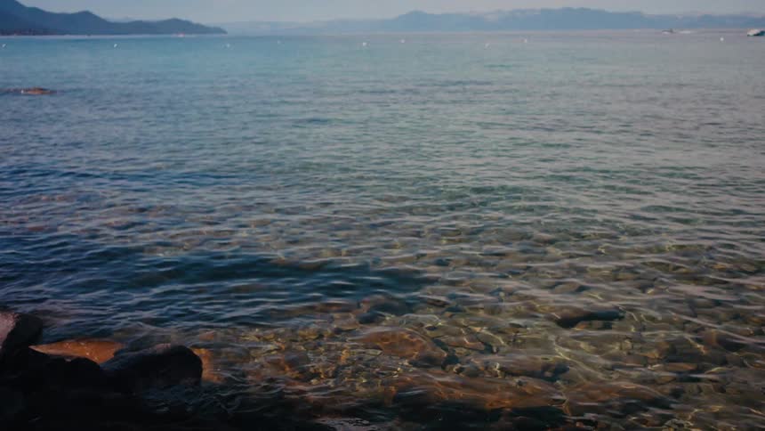 A slow zoom shot of the crystal clear waters of Lake Tahoe gently lapping on a rocky shore