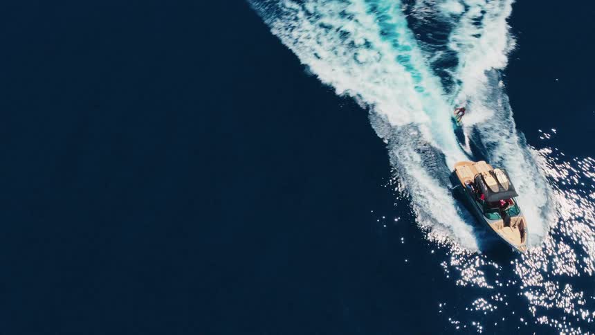 Dynamic aerial top-down shot of a wakesurfer riding the waves behind a motorboat on the deep blue sea
