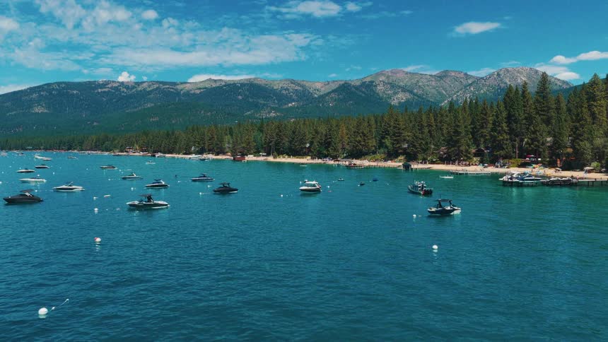 Scenic wide shot of numerous boats anchored in the clear turquoise waters of a mountain lake with a forested shoreline