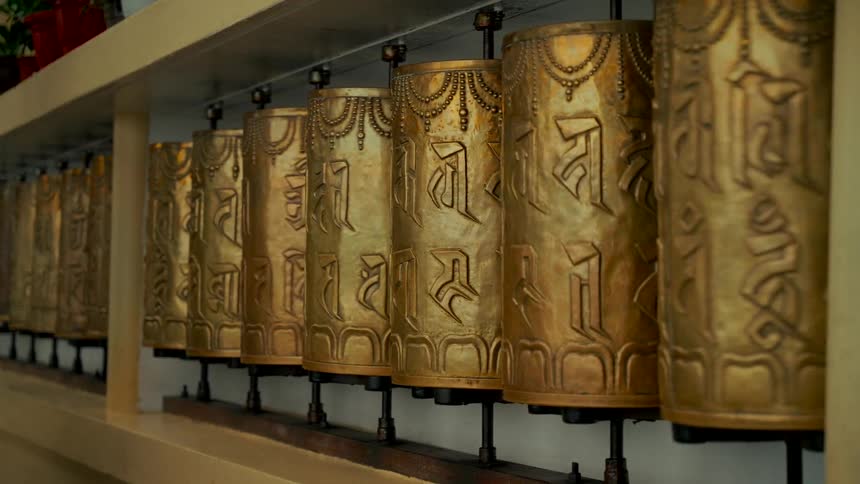 A row of ornate golden Tibetan Buddhist prayer wheels spin slowly in a monastery