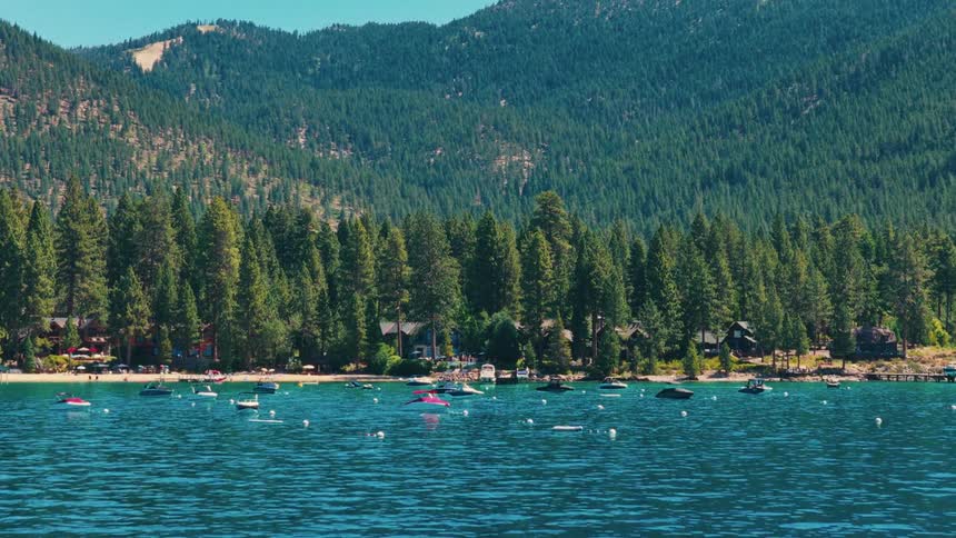 A serene view of numerous boats floating on the vibrant blue waters of a mountain lake, with a dense pine forest along the shoreline