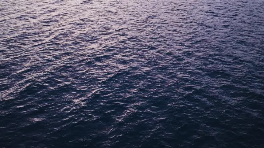 A serene, wide shot of the deep blue ocean surface rippling under the soft light of dawn or dusk