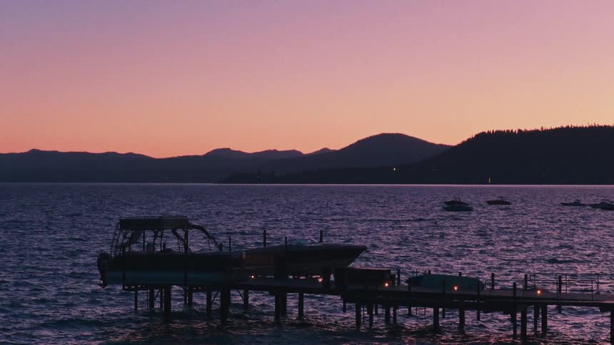 A tranquil mountain lake scene with a lighted pier and docked boats under a vibrant purple sunset sky