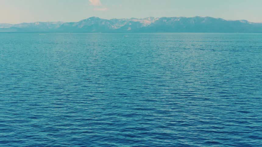 Calm blue waters of a vast lake ripple gently with a snow-capped mountain range visible on the horizon