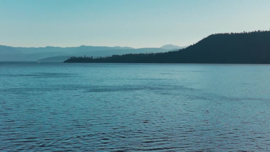 A serene wide shot of a vast blue lake with silhouetted mountains in the distance