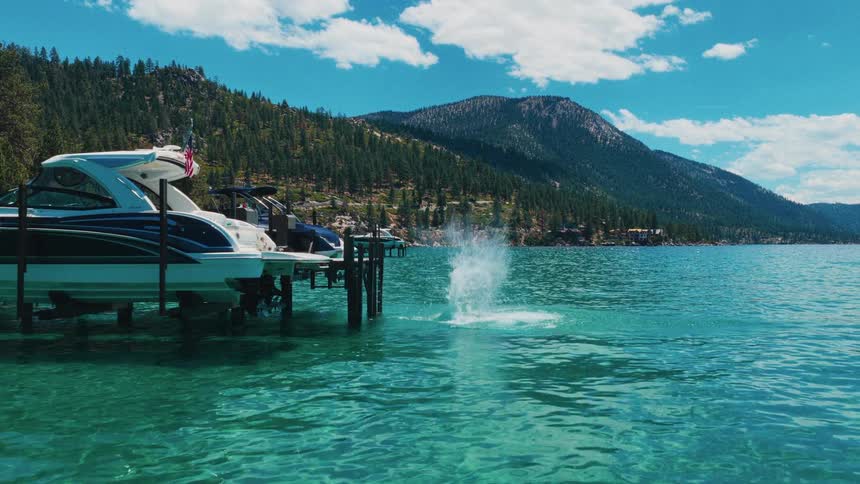 Slow motion view of friends having fun and jumping off a dock into a beautiful turquoise lake surrounded by mountains