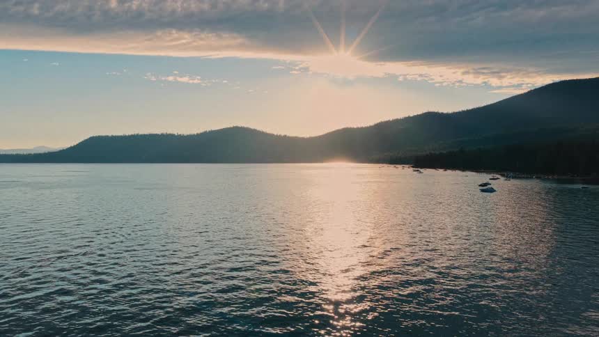 A stunning aerial view captures the serene beauty of a mountain lake at sunset, with the sun's golden light reflecting on the gentle waves