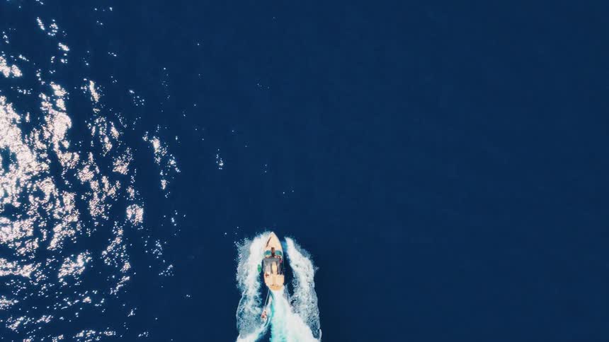 An aerial top-down view of a speedboat cruising across the deep blue sea, creating a prominent white wake
