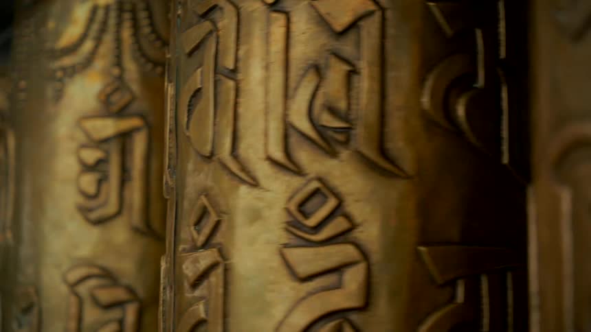 A close-up shot of ornate golden Tibetan prayer wheels with intricate mantras spinning in a continuous, meditative loop