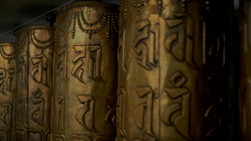 Ornate golden Tibetan prayer wheels inscribed with mantras spin slowly in a spiritual, meditative close-up