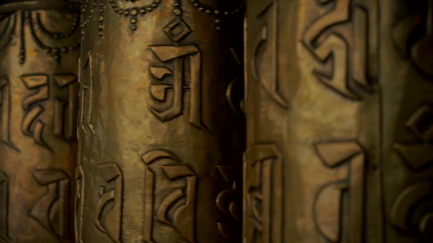 A close-up view of ancient golden Buddhist prayer wheels spinning slowly, revealing intricate Tibetan script