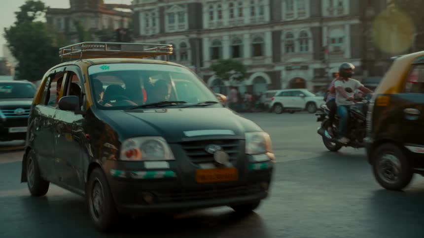 Black and yellow taxis navigate a busy intersection in Mumbai, India, during a hazy golden sunset