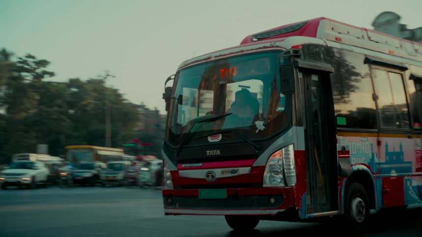 Slow motion tracking shot of a colorful tourist bus navigating a busy intersection in Mumbai, India at dusk