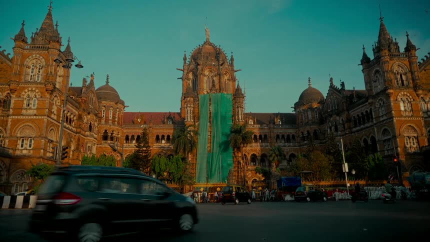 Busy city traffic flows past the historic Chhatrapati Shivaji Terminus train station in Mumbai, India at golden hour