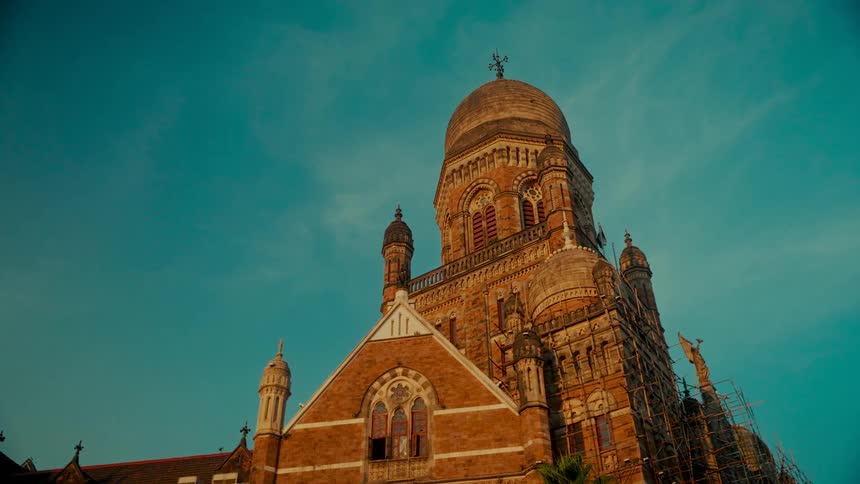Low-angle wide shot of the historic Brihanmumbai Municipal Corporation building in Mumbai, India, against a clear teal sky at dusk