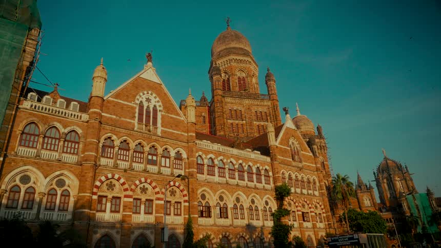 A low-angle, slow-panning shot of the historic Brihanmumbai Municipal Corporation building in Mumbai, India, illuminated by the warm light of sunrise