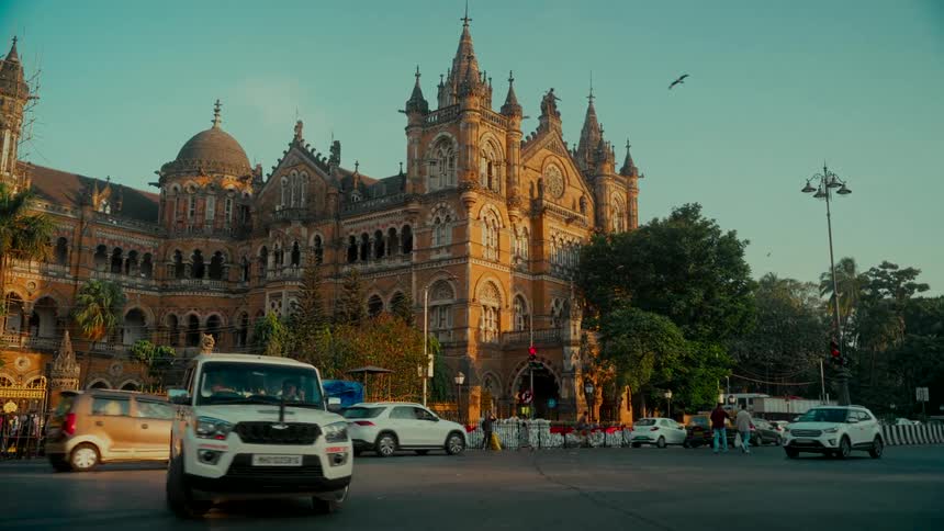 Traffic flows past the historic Chhatrapati Shivaji Maharaj Terminus in Mumbai during a warm, golden sunset