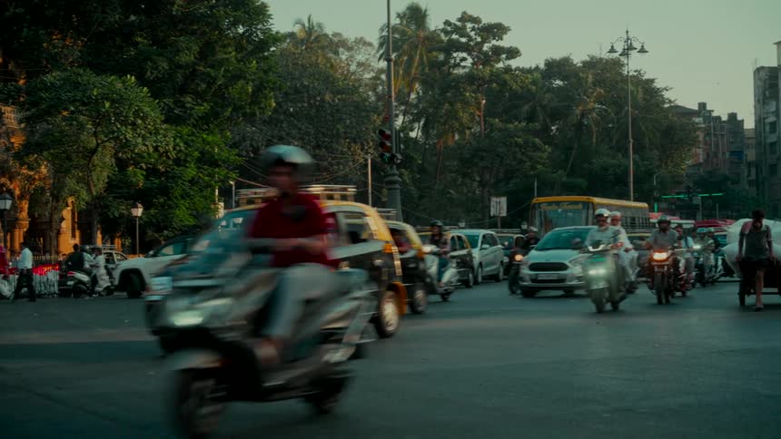 A slow-motion view of busy evening traffic with cars, motorcycles, and pedestrians navigating a city intersection in Mumbai, India