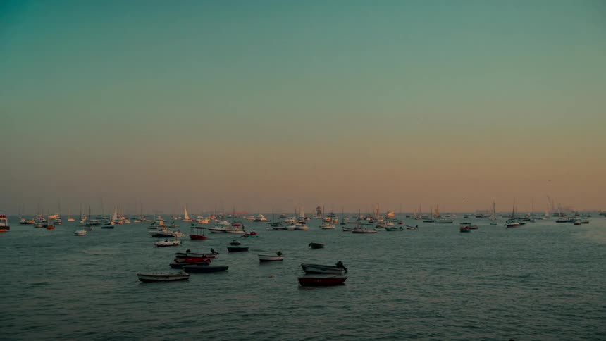 Dozens of boats rest on the gentle waves of the ocean during a serene and colorful sunset