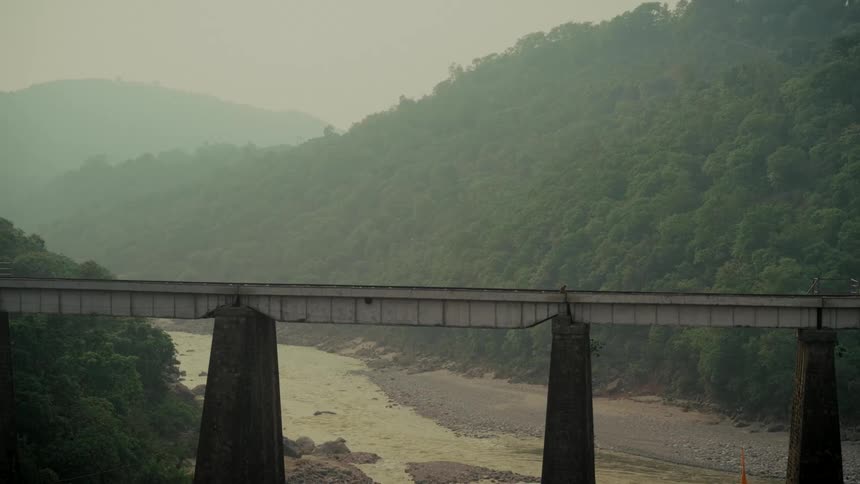A serene, static view of a bridge crossing a river through a hazy, green mountain valley