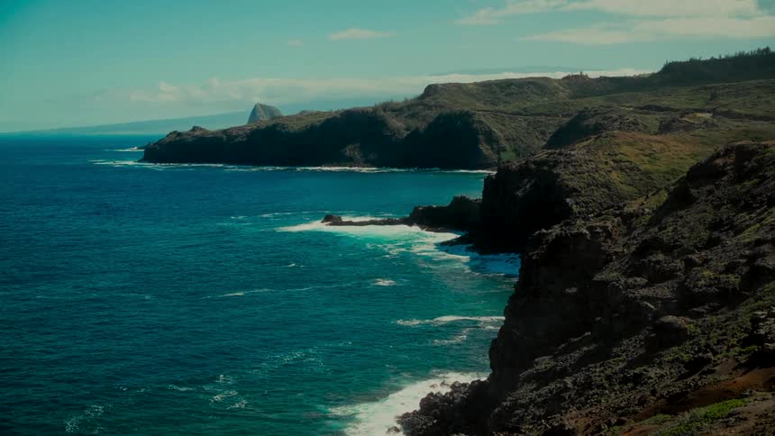 Sunlight illuminates the stunning volcanic cliffs and deep blue ocean along a tropical island coastline
