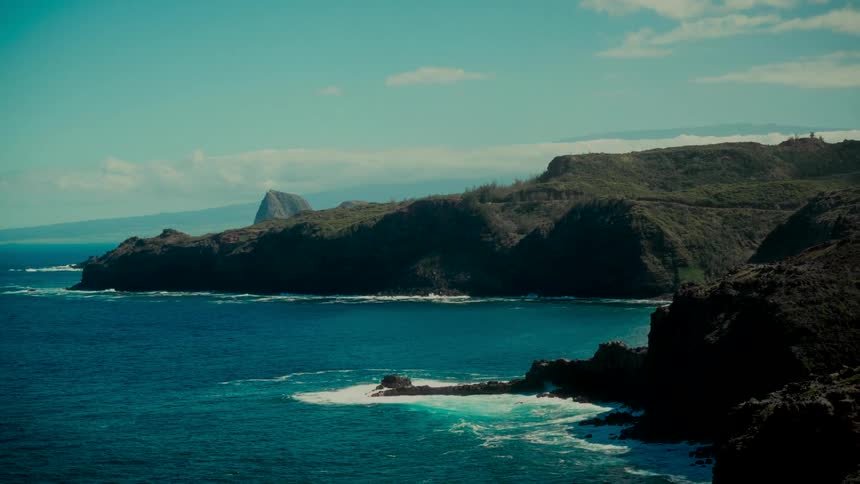 A scenic wide shot captures the lush green cliffs of a rugged coastline against the deep blue ocean