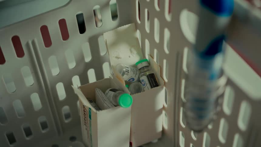 A close-up shot of several medical vials stored in cardboard boxes inside a white plastic basket