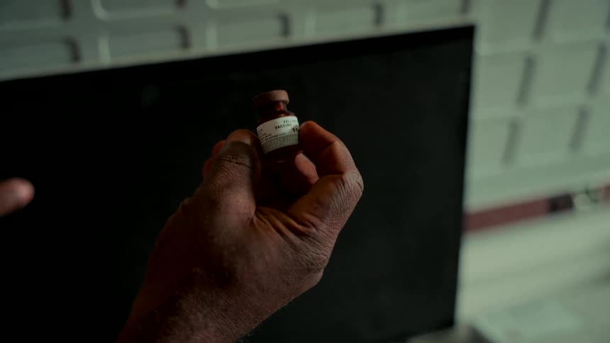 Close-up of a hand holding a vial of yellow fever vaccine in a sterile, futuristic laboratory