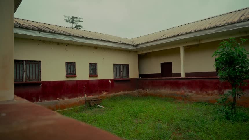 A static shot of a weathered building's empty courtyard with overgrown grass on a gloomy, overcast day