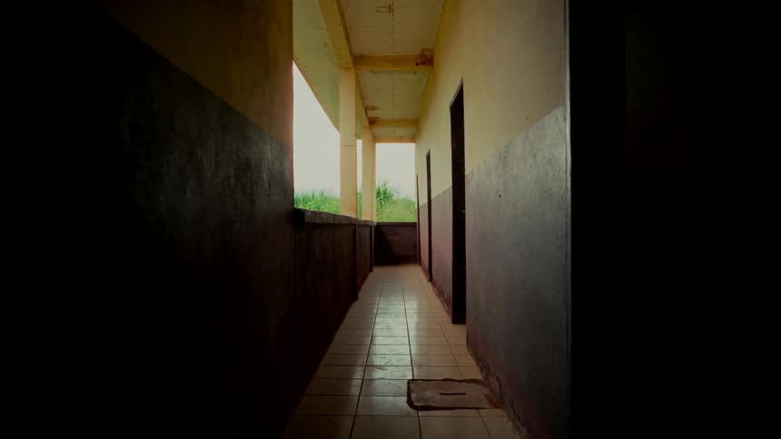 A dark and eerie hallway in an abandoned building slowly fades to black