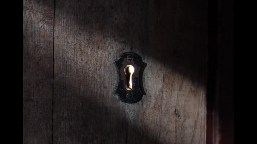 Light flickers through the keyhole of a rustic wooden door as shadows pass by, creating a mysterious atmosphere